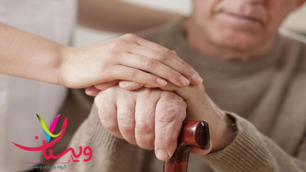بیمار مبتلا به پارکینسون نشسته، و پرستار با محبت دست او را گرفته است